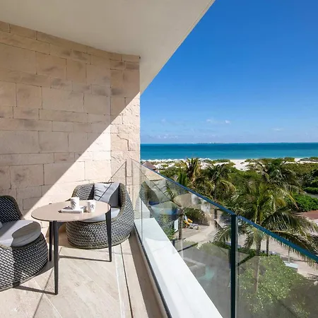 Trs Coral Hotel (Adults Only) Cancun Amenities photo The photo shows a balcony with a view of a beautiful tropical beach. The balcony is made of light-colored stone and has a glass railing. There are two wicker chairs with cushions and a small round table with a tray on it. The chairs are facing the oc