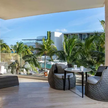 Trs Coral Hotel (Adults Only) Cancun Interior photo The photo shows a stylish outdoor lounge area, likely part of a resort or hotel. The space is covered by a wide, open doorway or patio, offering a view of a tropical scene. 

The flooring is light-colored wood, and the area is furnished with comforta