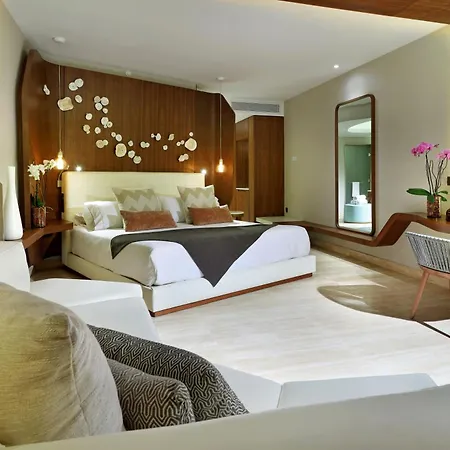 Trs Coral Hotel (Adults Only) Cancun Room photo The photo shows a modern and luxurious bedroom with a warm and inviting atmosphere. The room features a large bed with a white headboard and a dark gray throw blanket. The bed is adorned with several pillows in shades of beige and brown. 

The walls 