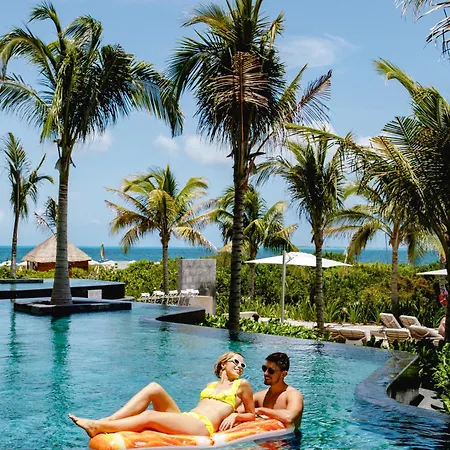 Trs Coral Hotel (Adults Only) Cancun Swimming Pool photo The photo shows a beautiful tropical resort scene. The foreground features a large, inviting swimming pool with clear blue water. Several palm trees with lush green fronds surround the pool, creating a relaxed and luxurious atmosphere. 

In the middl