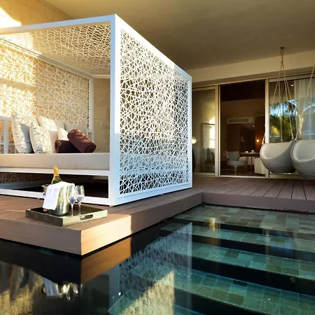 Trs Coral Hotel (Adults Only) Cancun Interior photo The photo shows a luxurious outdoor relaxation area, likely part of a resort or high-end home. The main focus is a white, intricately designed daybed with a cushioned mattress and several pillows, positioned on a raised wooden platform. The daybed is