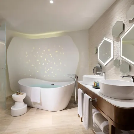 Trs Coral Hotel (Adults Only) Cancun Facilities photo The photo shows a luxurious bathroom with a modern and minimalist design. The focal point is a large, white, oval-shaped bathtub with a curved backrest, filled with light blue water. The bathtub is positioned against a white wall adorned with subtle,