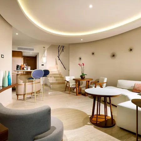 Trs Coral Hotel (Adults Only) Cancun Toilets photo The photo shows a bright and modern lounge area, likely in a hotel or resort. The space is characterized by a curved, light-colored wall and a light beige tiled floor. 

In the foreground, a light gray armchair with a rounded back is partially visibl