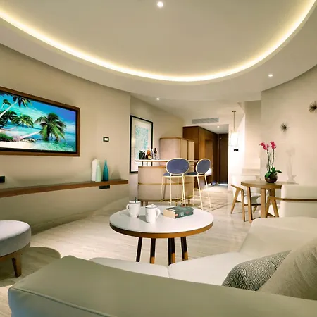 Trs Coral Hotel (Adults Only) Cancun Interior photo The photo shows a modern and bright living area with a relaxed, beach-inspired vibe. The walls are a warm beige, and the flooring is a light-colored wood. A large flat-screen TV is mounted on the wall, displaying a vibrant image of a tropical beach w